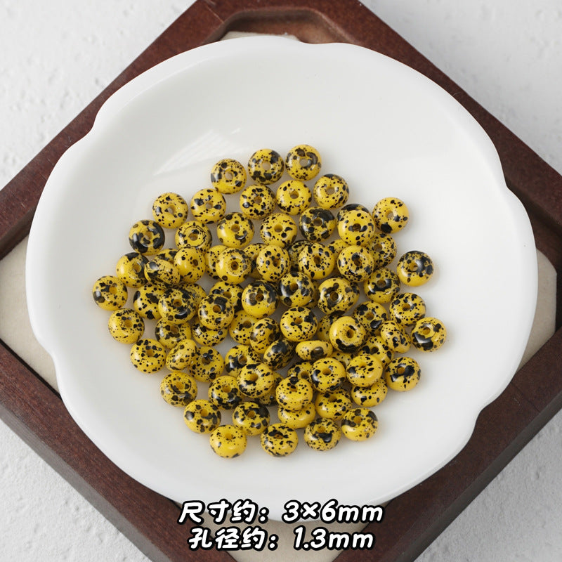 Yellow and black speckled Picasso glass abacus beads in a white dish on dark wooden tray.