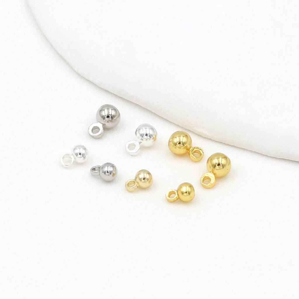 Silver and gold ball charms with loop backs on a white background with a curved fabric accent