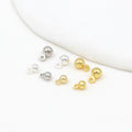 Silver and gold ball charms with loop backs on a white background with a curved fabric accent