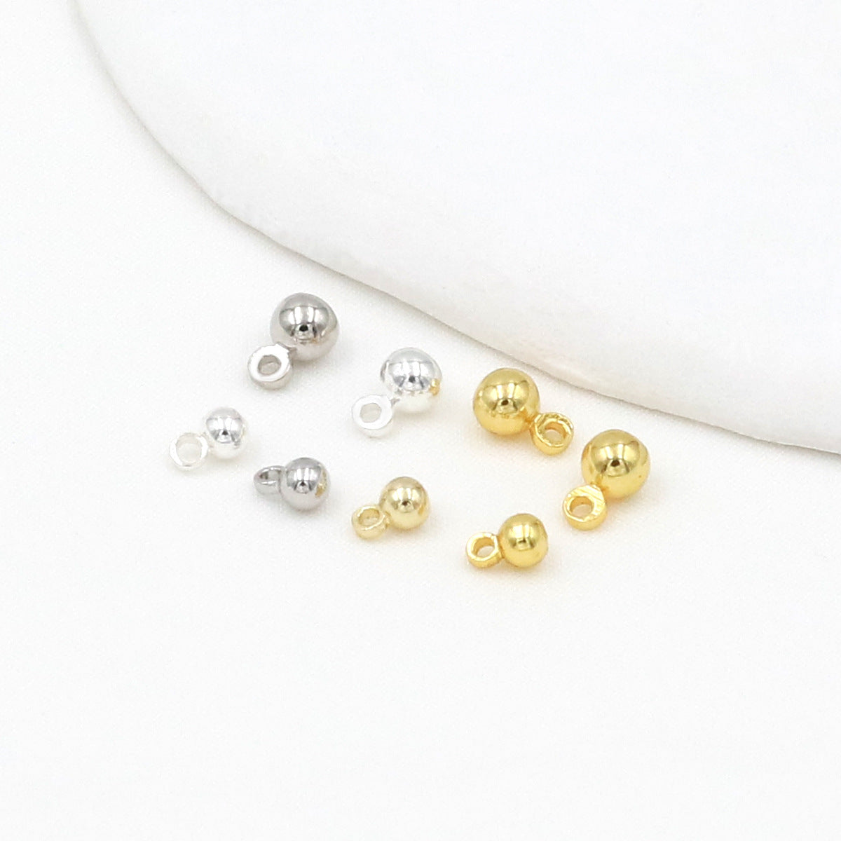Silver and gold ball charms with loop backs on a white background with a curved fabric accent