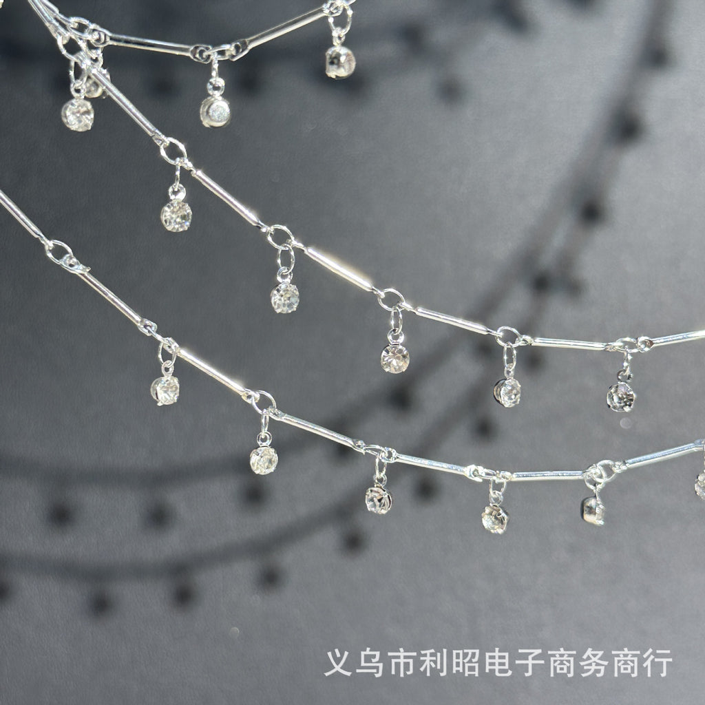 Silver chain necklace with dangling clear rhinestone charms, shown in a close-up studio-style shot on a dark gray background.