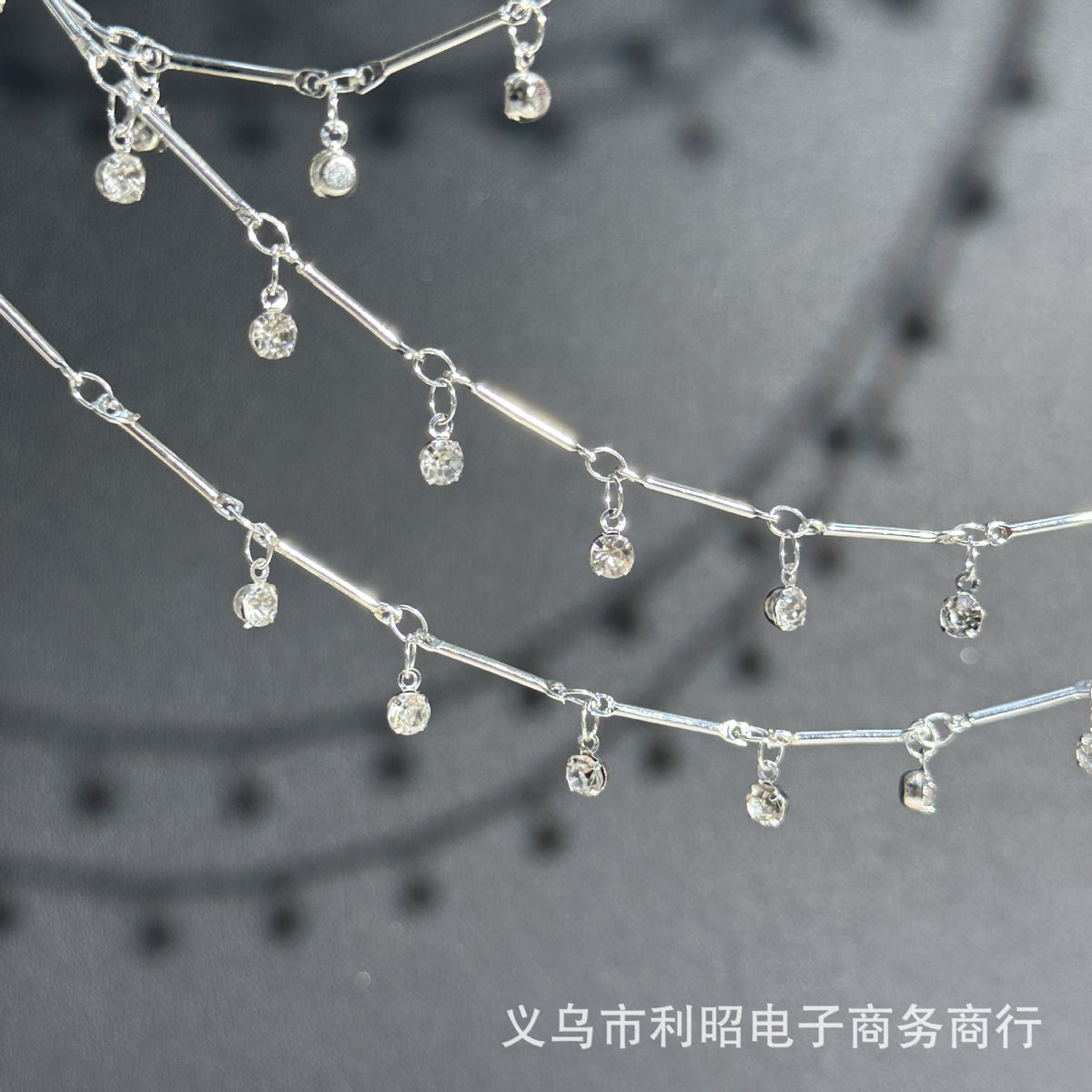 Silver chain necklace with dangling clear rhinestone charms, shown in a close-up studio-style shot on a dark gray background.