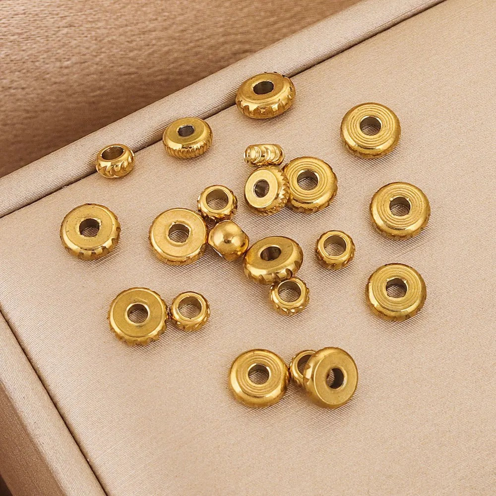 Gold-plated diamond-cut stainless steel abacus spacer beads on a beige fabric surface