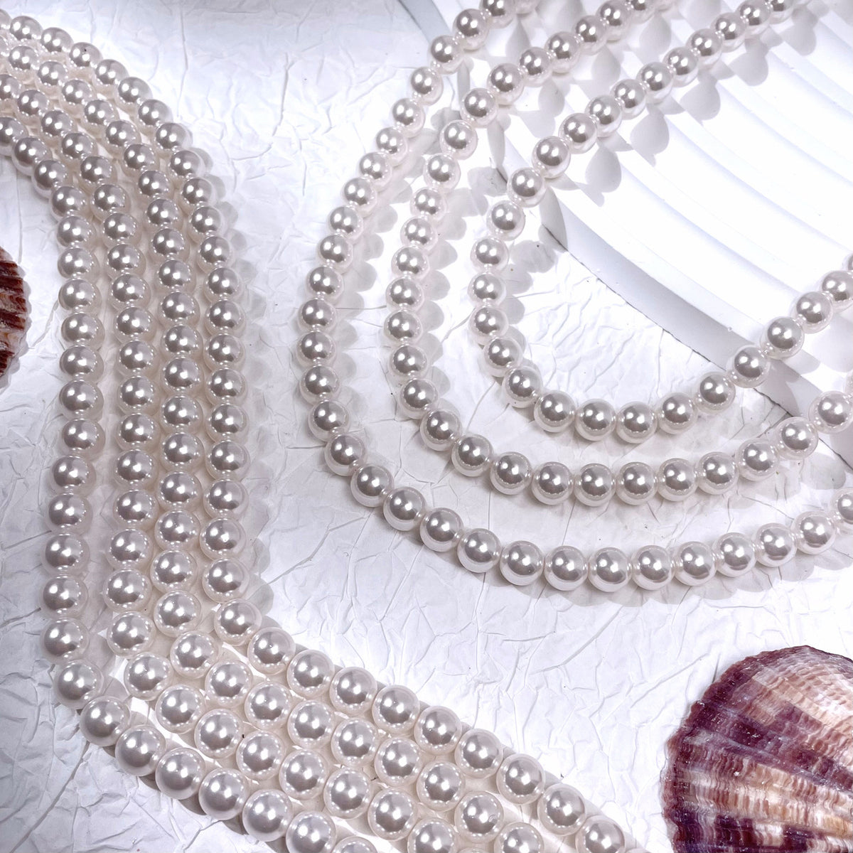 Multiple strands of white glass pearl beads in flowing curves with seashells
