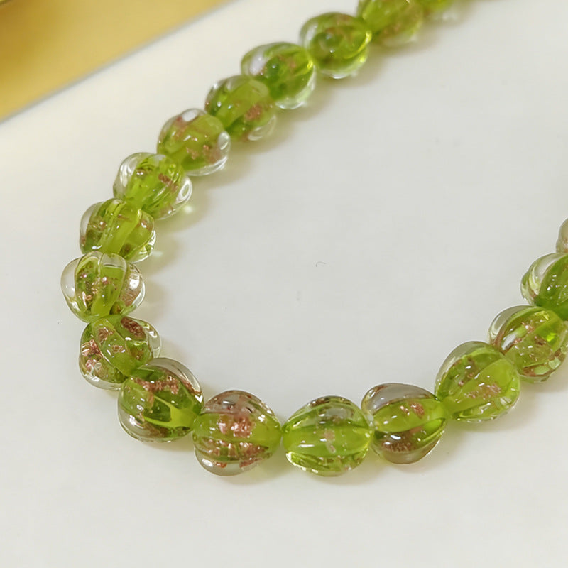 Bracelet of translucent green lantern glass beads with coppery flakes on a white surface