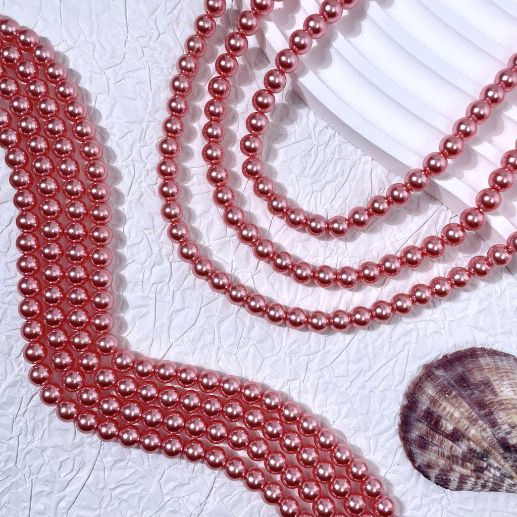 Rose pink glass pearl strands on textured white surface with seashell