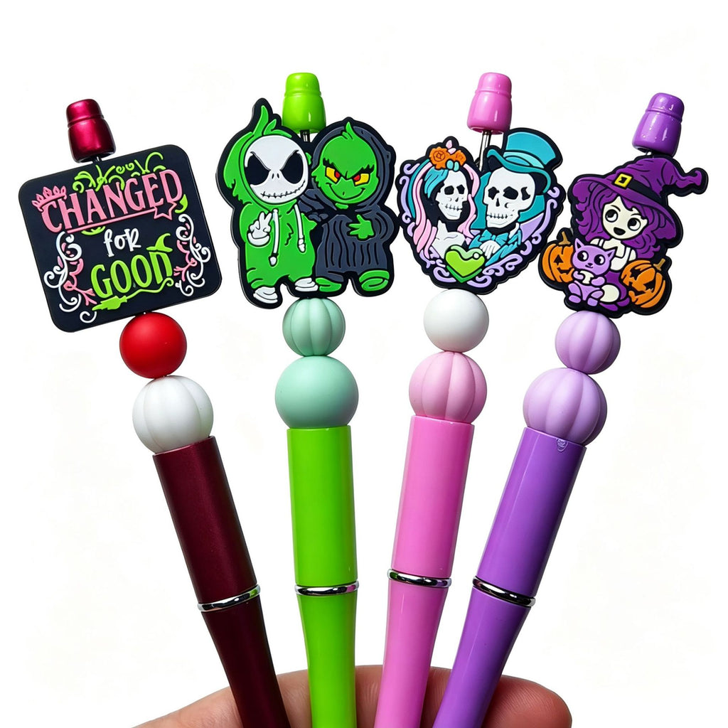 Four beaded pens with Halloween silicone focal toppers including skeleton, witch, and Changed for Good sign designs