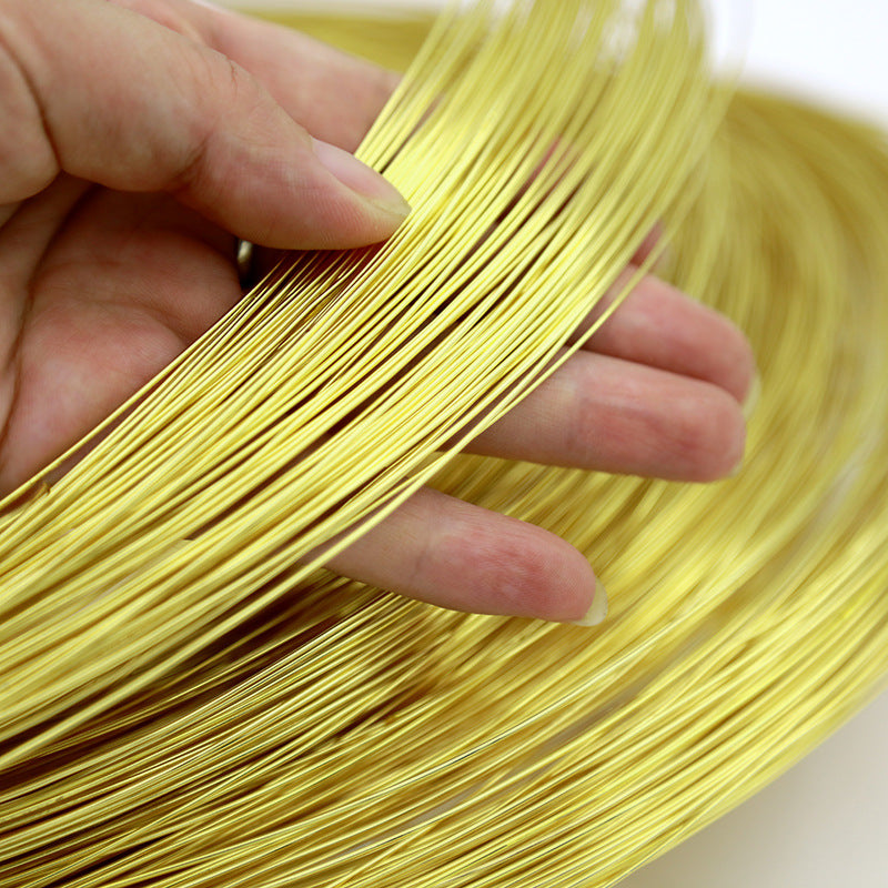 A close-up of a hand holding a coiled bundle of thin metallic gold wire against a light neutral background.