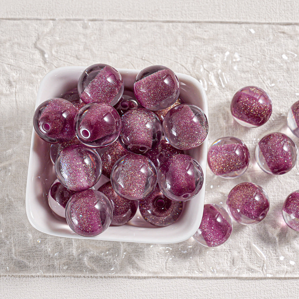 Magenta-purple glitter round beads in a white dish and scattered on textured surface