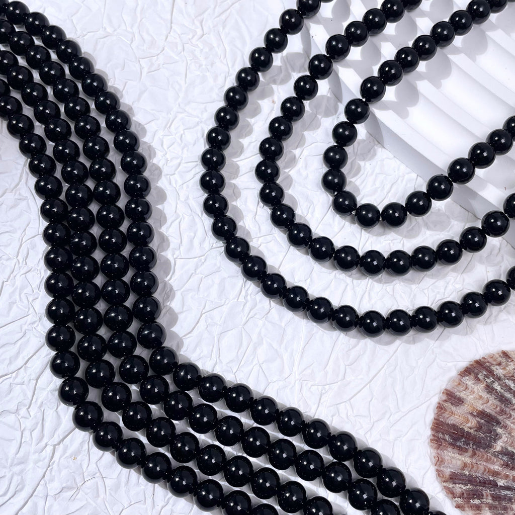 Three strands of glossy black glass pearl beads on white textured surface with seashell prop