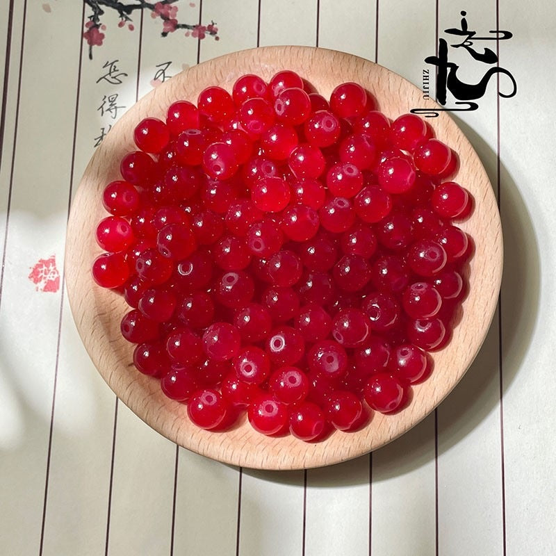 Red translucent round beads in a light wood bowl on cream background with calligraphy
