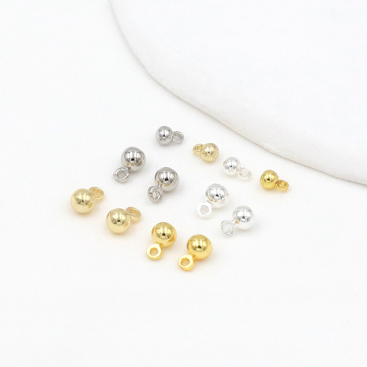 Small gold and silver ball beads with loop ends arranged on a white background with a curved white prop