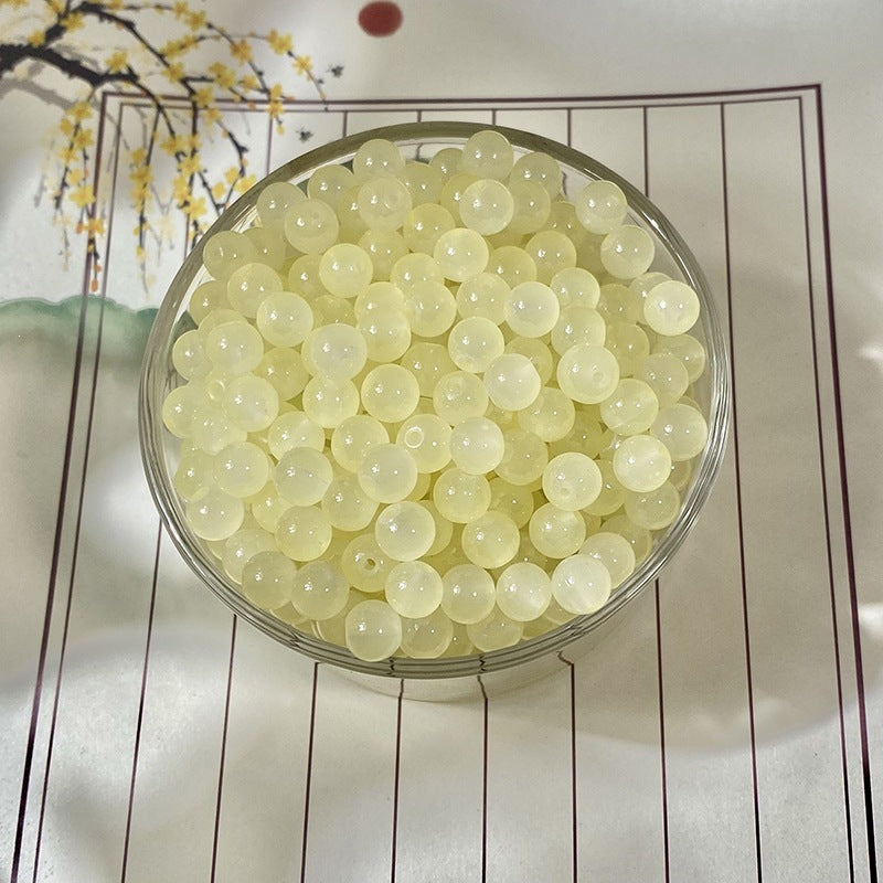Pale yellow round beads in a clear container on white surface with floral decorations