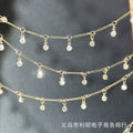 Gold chain waist beads with dangling clear rhinestone charms, arranged in three horizontal rows against a dark gray background.