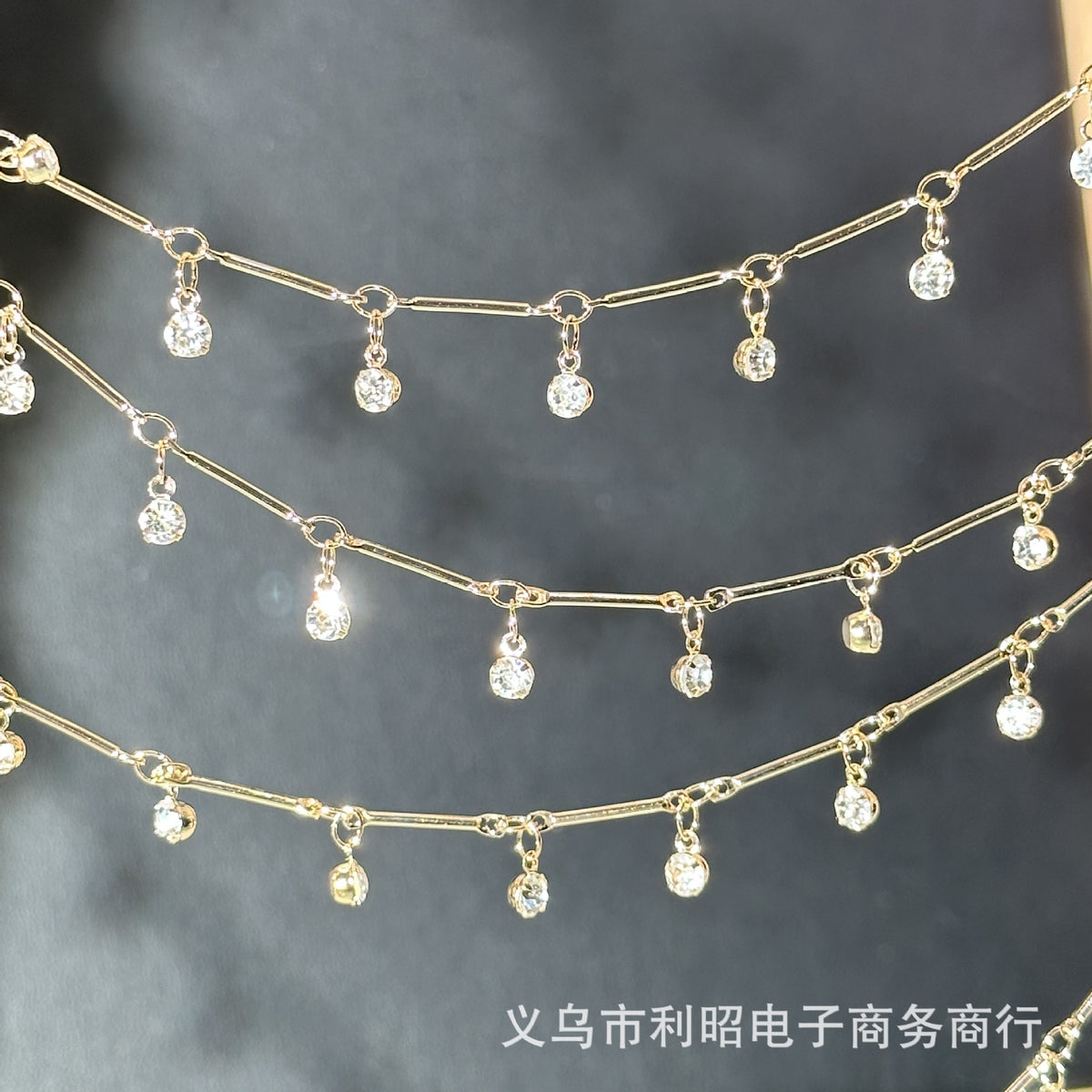 Gold chain waist beads with dangling clear rhinestone charms, arranged in three horizontal rows against a dark gray background.