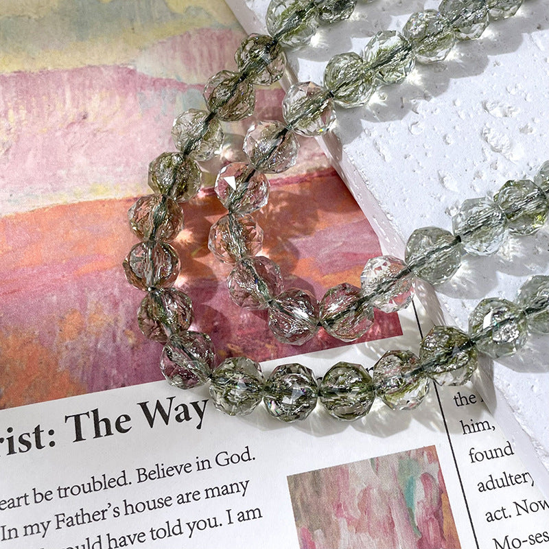 Strand of faceted clear glass beads with greenish-gray crackle interiors over printed paper and a white textured surface