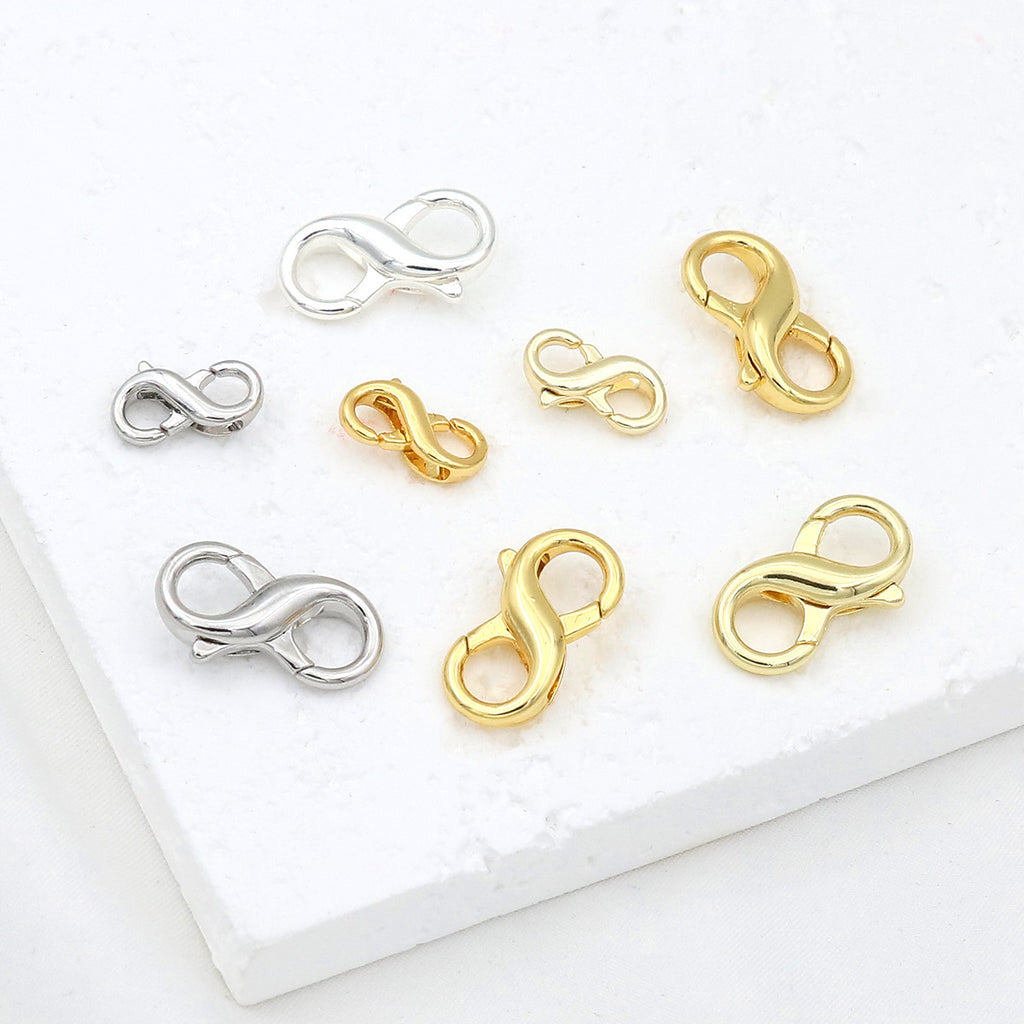 Eight figure-eight lobster clasps in two sizes and polished silver and gold finishes on a white textured surface