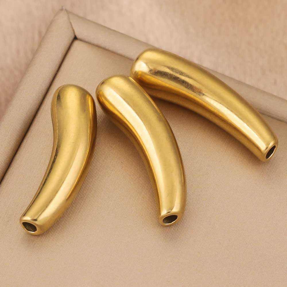 Three curved metallic gold beads with hollow centers, displayed on a beige textured fabric surface.