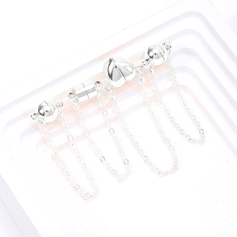 Four silver magnetic clasps with safety chains in ball, cylinder, and heart shapes with dangling chains on a white tray