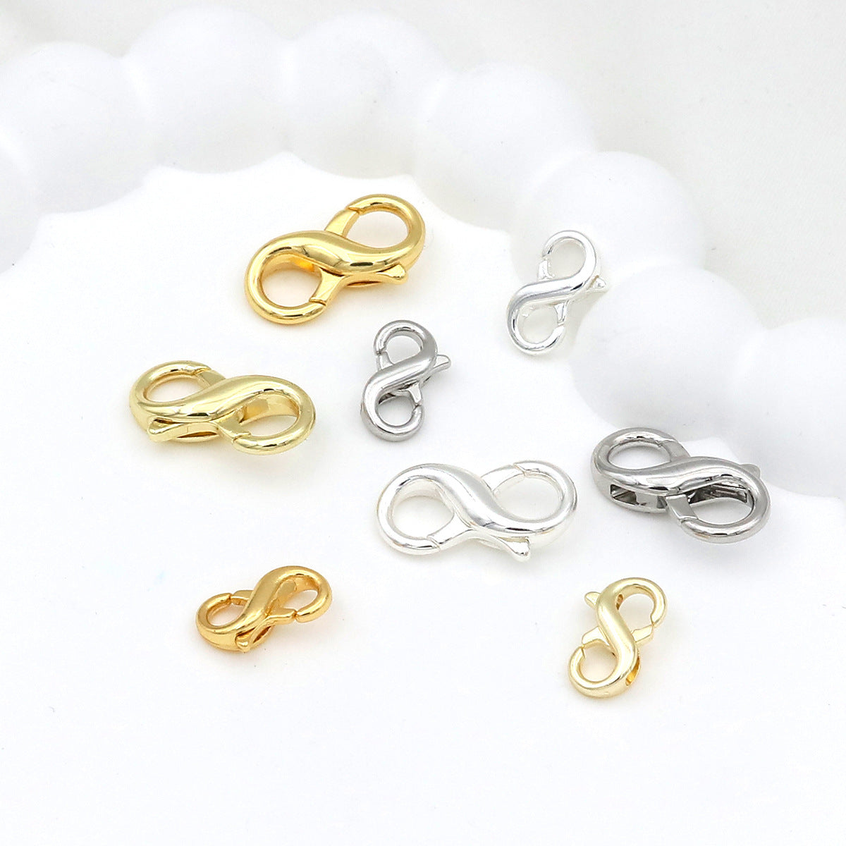 Six small figure-eight lobster clasps in gold and silver finishes on white with a cloud-like shape behind
