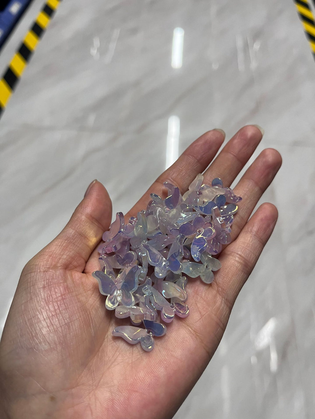 Hand holding pile of small iridescent purple and blue butterfly acrylic beads against gray marble floor