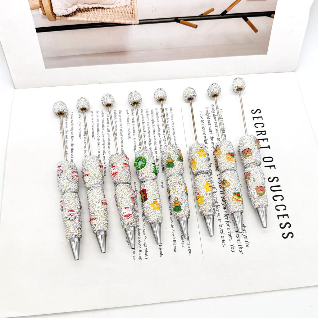 Nine rhinestone ballpoint pens with colorful Christmas cartoon designs on an open book.