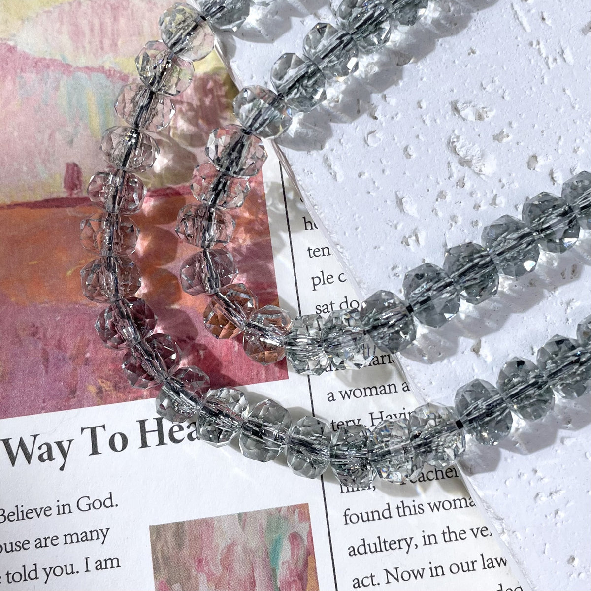 Strands of clear smoky-grey faceted crystal beads on a printed book page and textured white surface