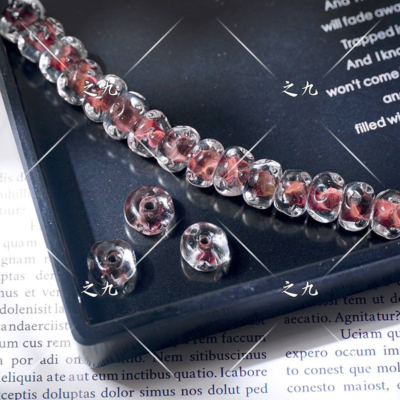 Clear lampwork glass beads with red swirl patterns on a black tray, loose beads