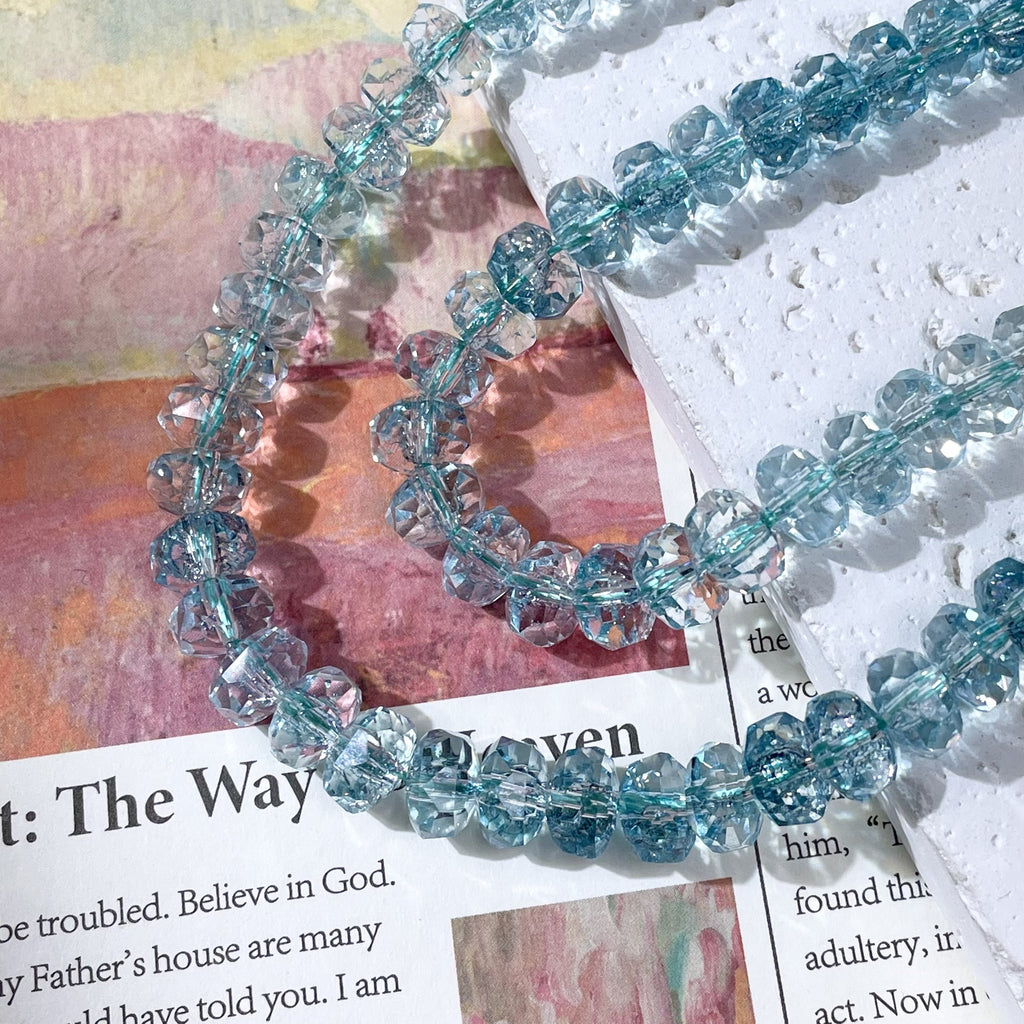 Strands of faceted light blue crystal beads on a printed page and white textured paper