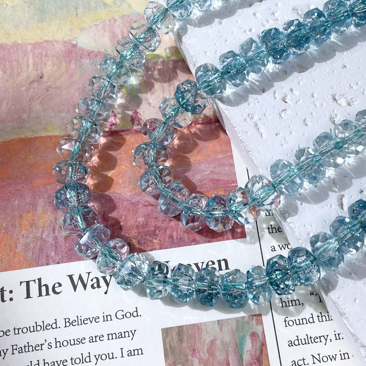 Strands of faceted light blue crystal beads on a printed page and white textured paper