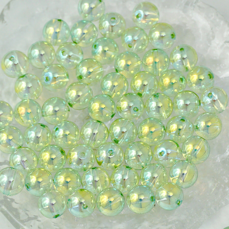 A pile of round, iridescent glass beads with a pale yellow-green hue and subtle green flecks, resting on a clear, textured surface.