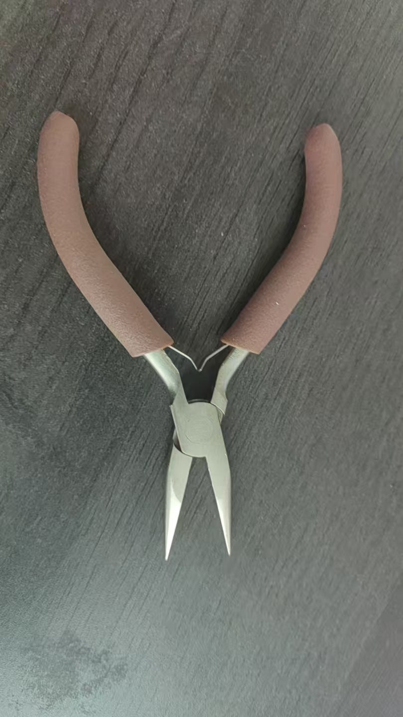 Brown-handled needle-nose jewelry pliers with silver jaws on gray surface