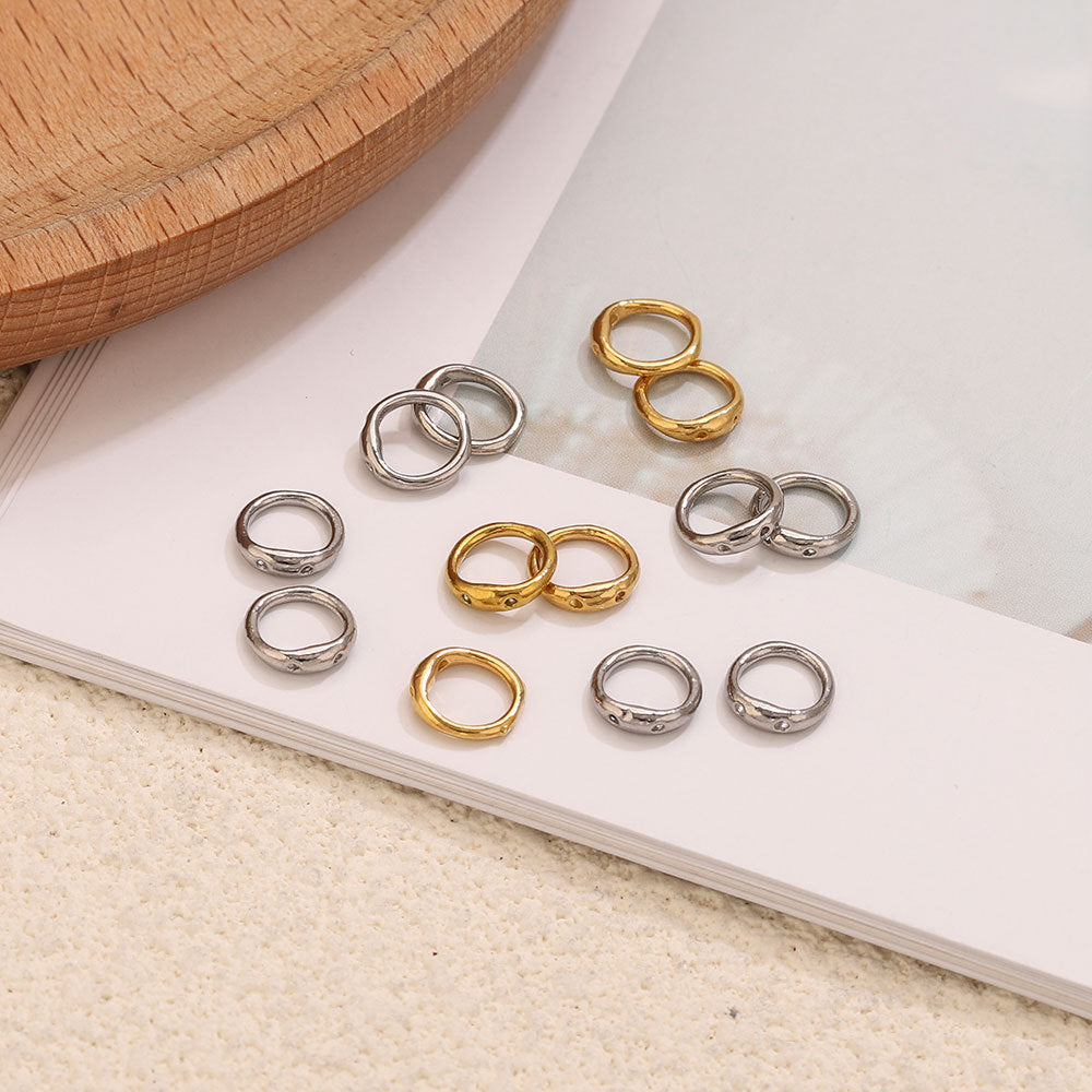 Nine gold and steel color double-ring spacer connectors arranged on white book page with wooden tray
