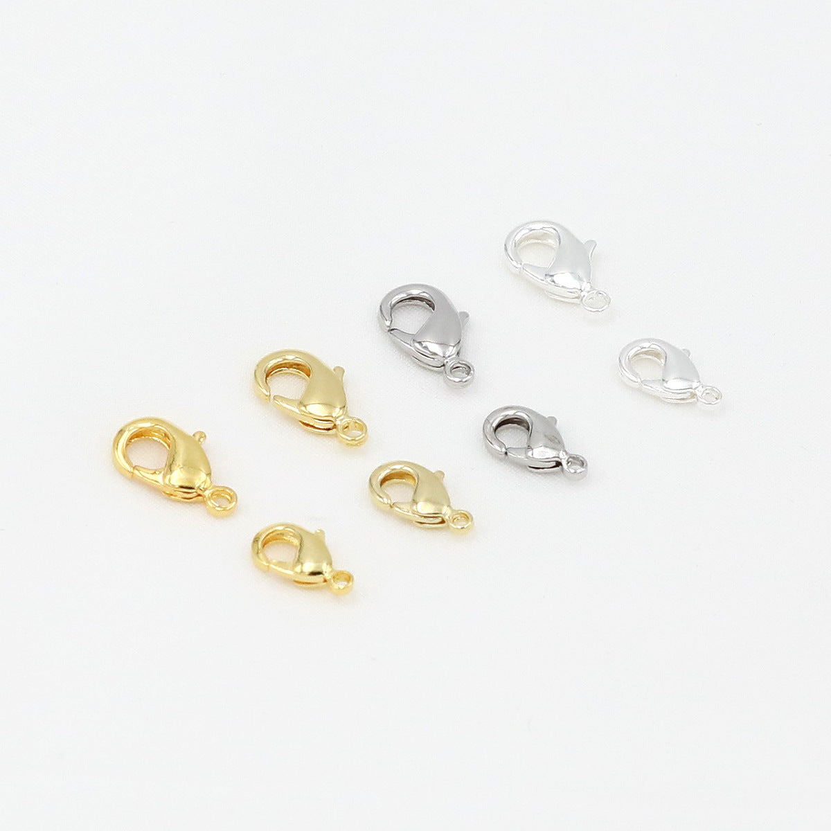 Eight gold and silver teardrop lobster clasps arranged on a white background