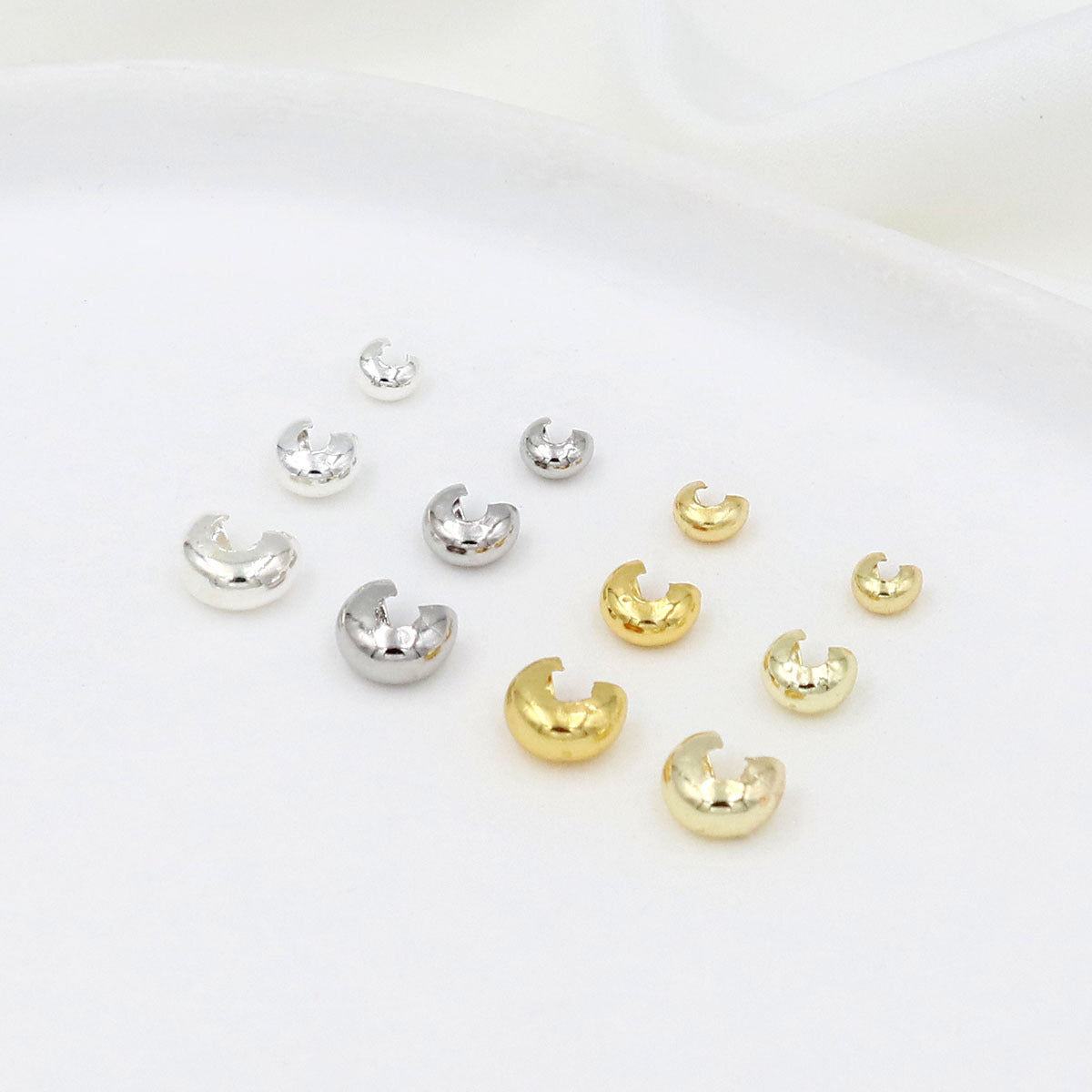 Nine C-shaped crimp bead covers in silver and gold finishes arranged on a white background