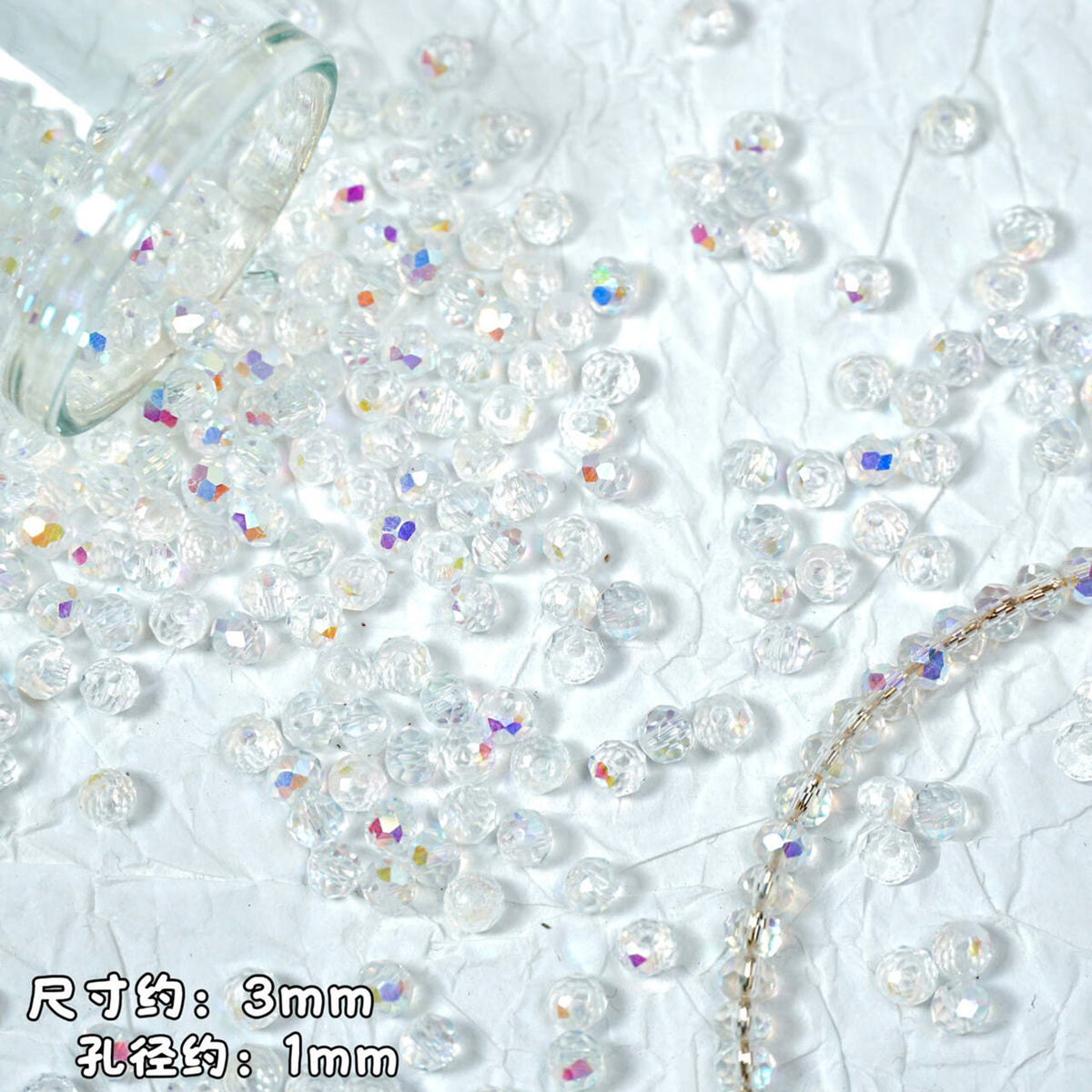 Clear round acrylic beads with iridescent rainbow reflections, scattered on a white textured background with a glass container spilling more beads and a beaded strand.