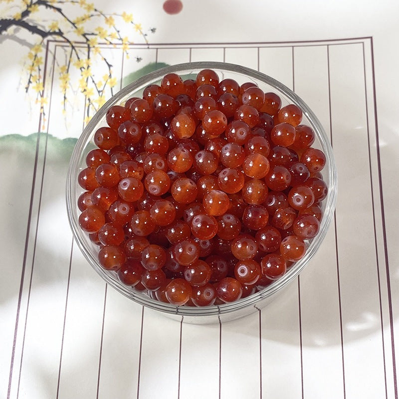Glossy red-orange round beads in a clear glass bowl on decorative mat