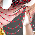 Hand holding draped strands of black metal chain with small red enamel heart beads