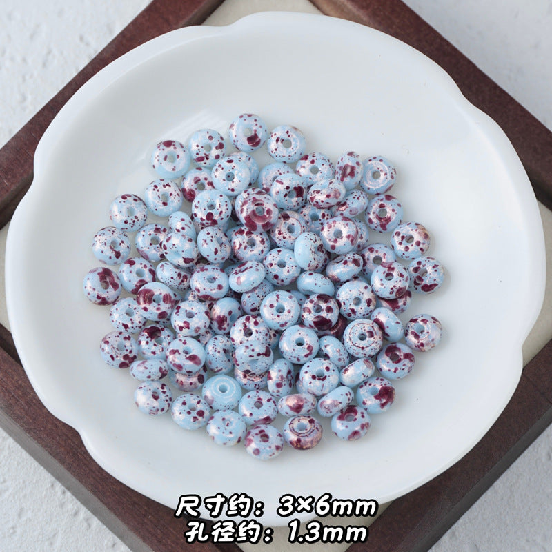 Light blue and white speckled Picasso glass abacus beads piled in a white scalloped dish.
