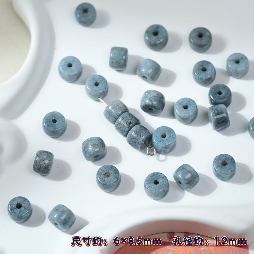 Blue-gray stone cylinder porcelain beads on white, one strand threaded on needle