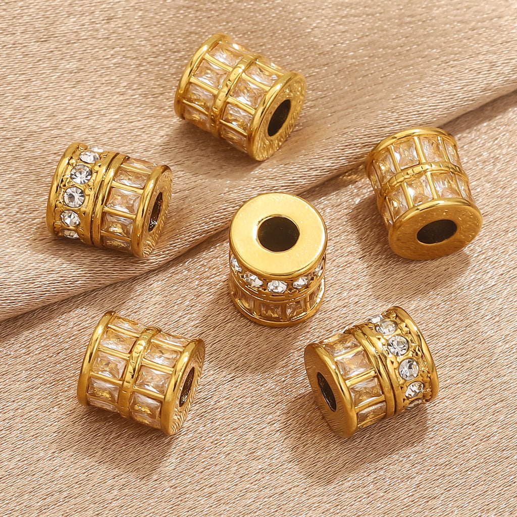 Five gold cylindrical bead spacers with clear rhinestone accents, arranged on a beige textured fabric background.