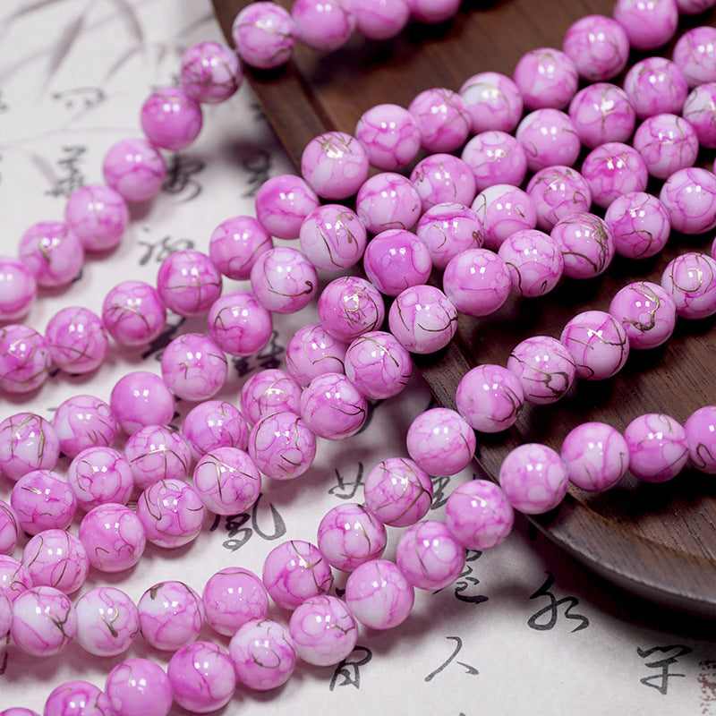 Pink and white marbled porcelain beads with dark veining draped over a wooden tray