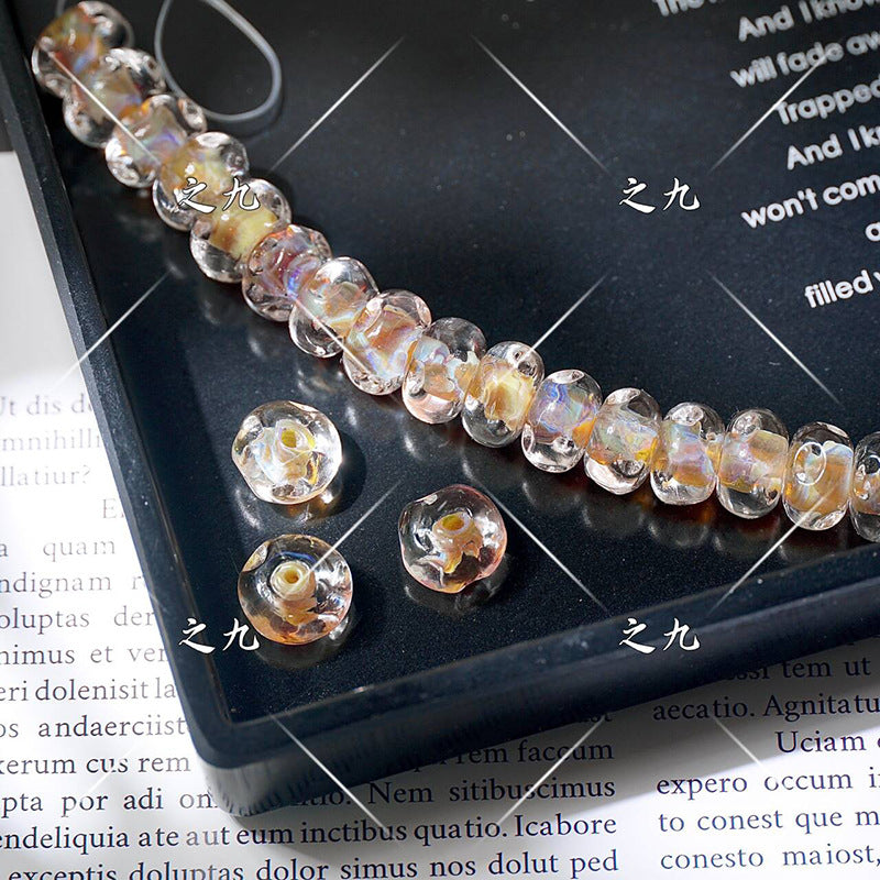 Iridescent clear lampwork glass beads with pink and orange shimmer on a black tray, loose beads