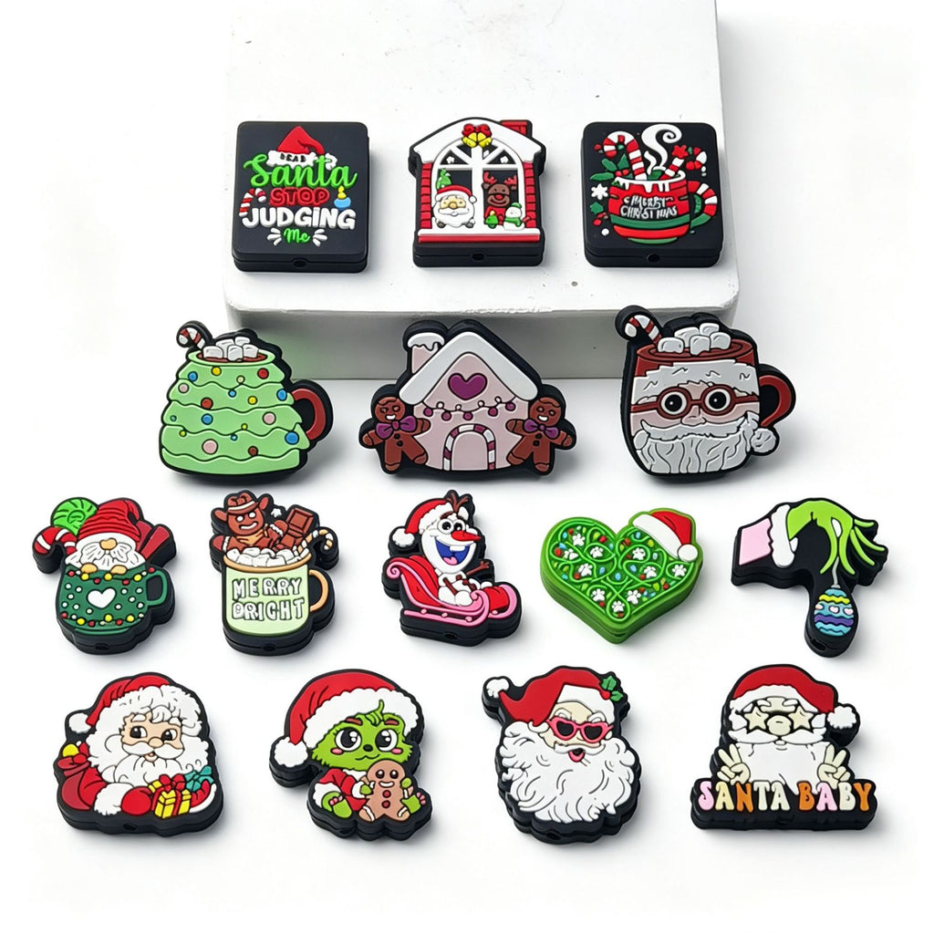 Fifteen Christmas-themed silicone focal beads arranged on a white surface in assorted festive designs