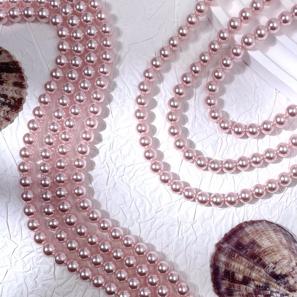 Pink glass pearl bead strands on textured white surface with seashells