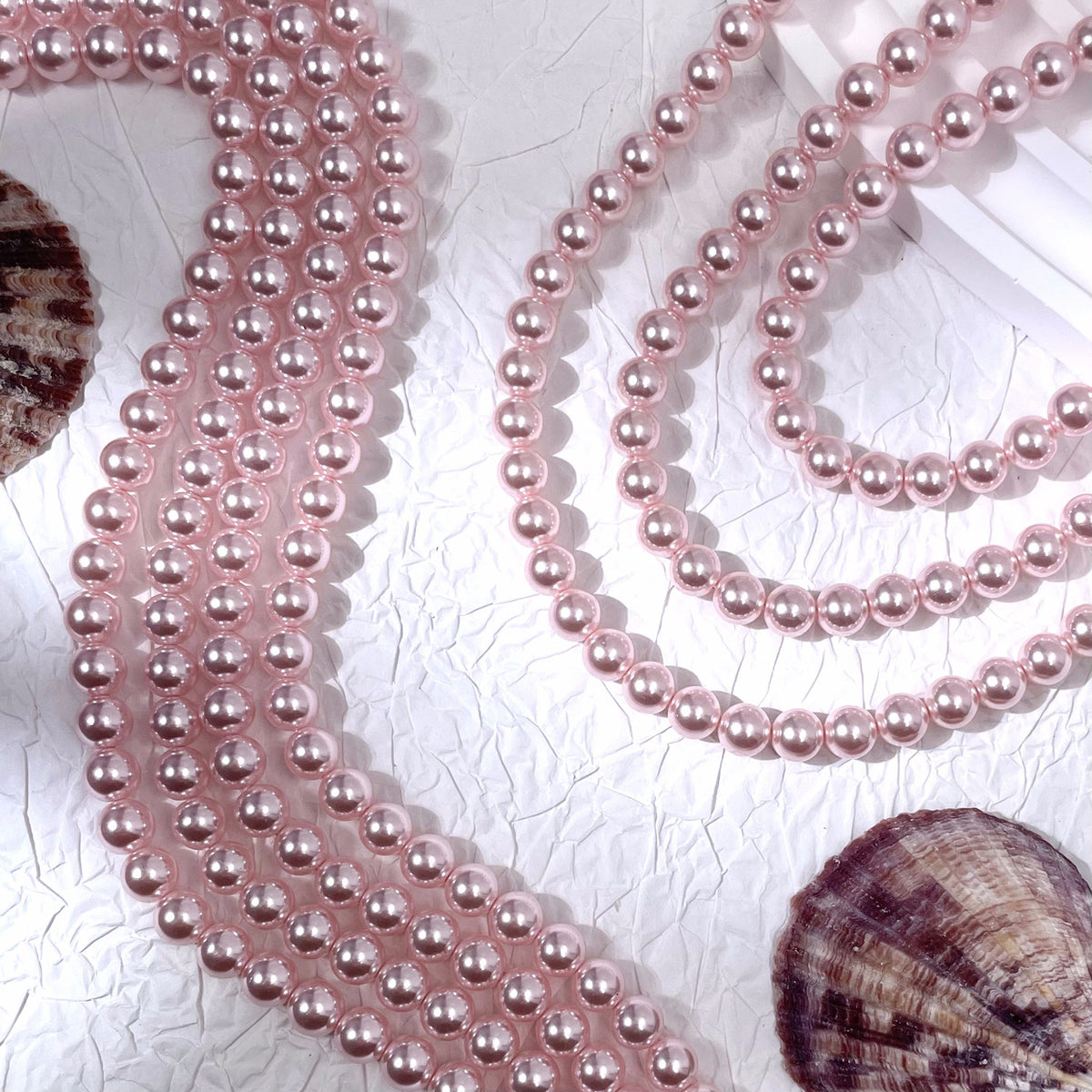 Pink glass pearl bead strands on textured white surface with seashells