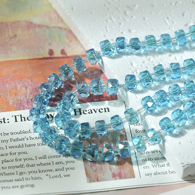 Light blue faceted glass beads threaded on clear cords arranged in loops over printed paper and a textured white background