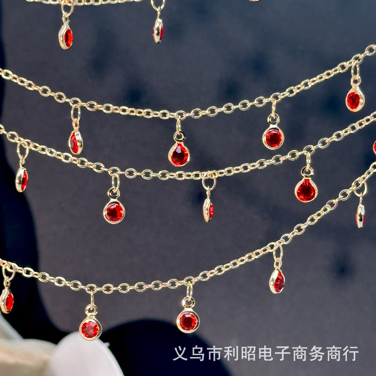 Gold chains with dangling red teardrop gemstones, close-up on dark background.