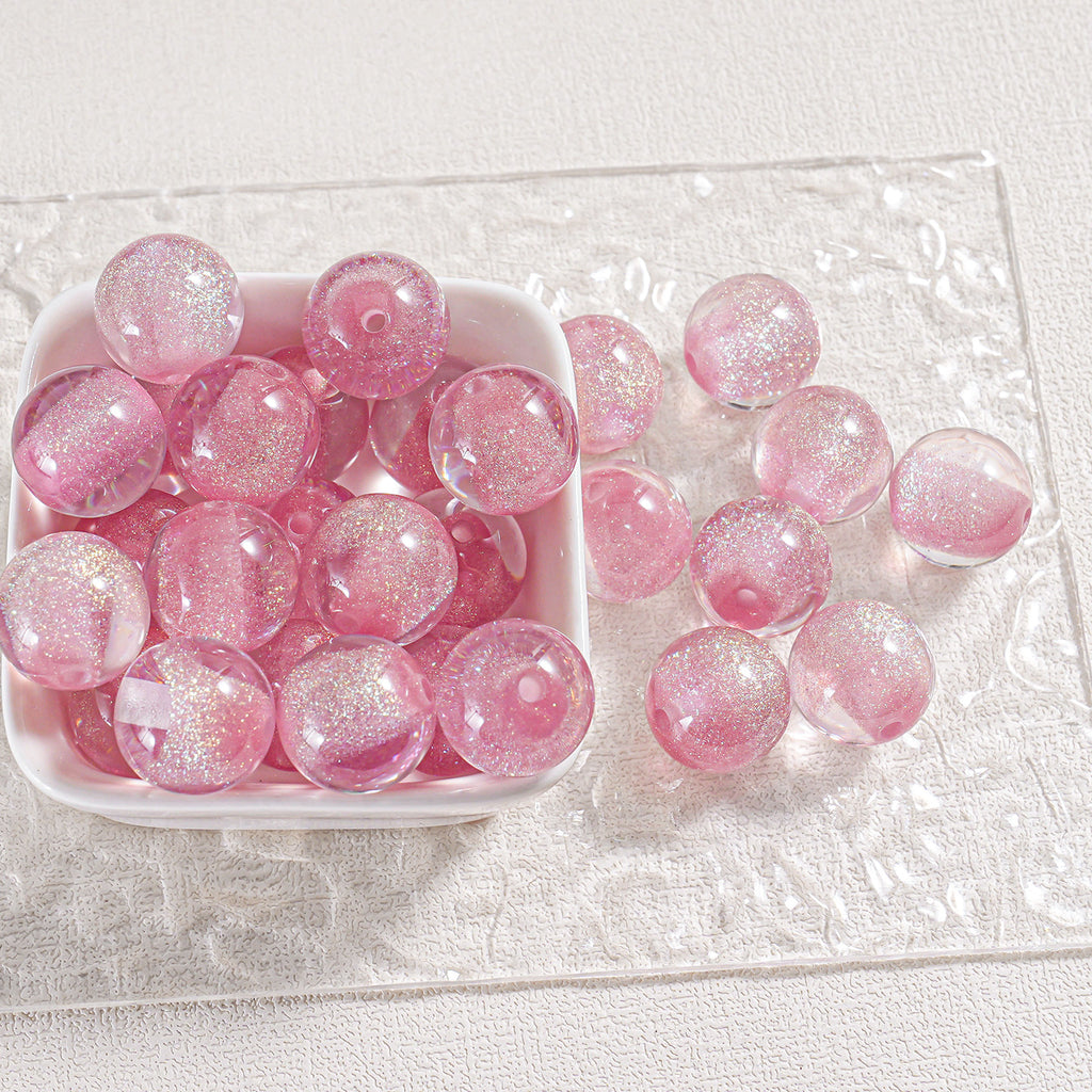 Pink glittery round beads in a white dish with loose beads on a clear textured mat