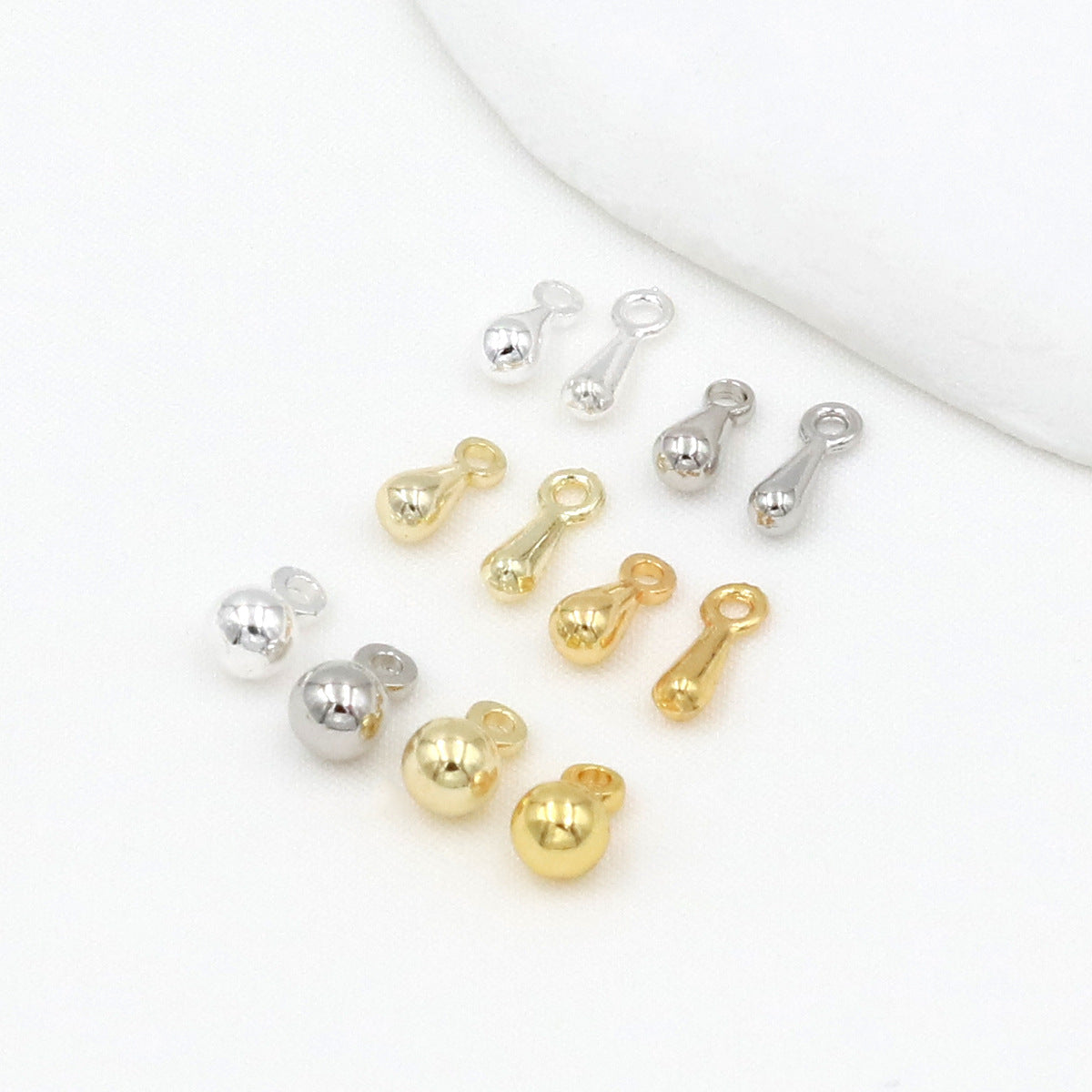 Gold-plated teardrop and ball charms in gold and silver tones arranged on a white surface